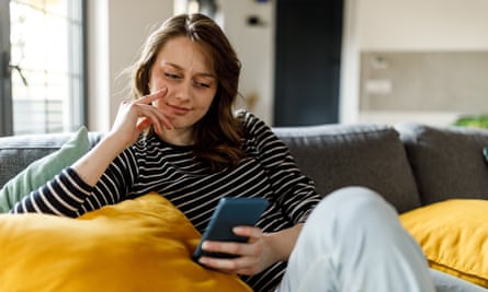 Young woman lounging on the sofa and scrolling online via smart phone
