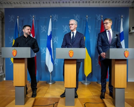 Zelenskiy, Store and Stubb stand at podiums during a press conference with national flags behind them