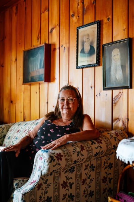 A middle-aged woman sits on a couch surrounded by old photos.