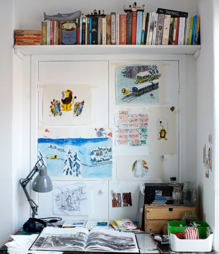 An open book on a desk, with illustrations taped to the wall