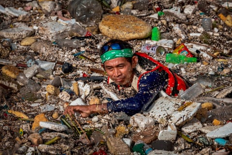 A worker wades through a sea of floating garbage that is clogging a river