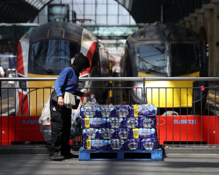 A woman takes a bottle of water from a stack in front of two train locomotives