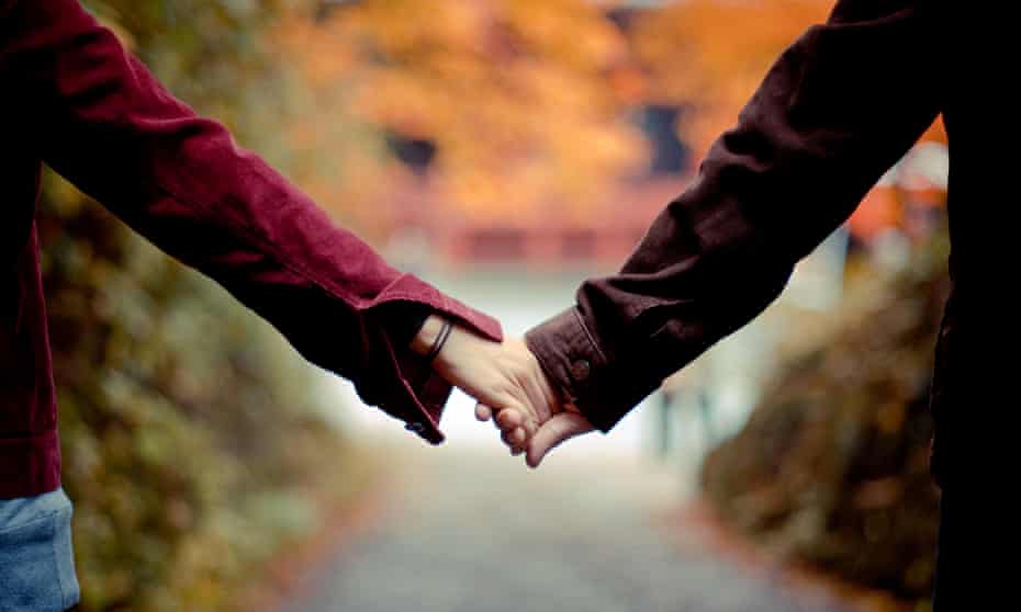 Couple holding hands while walking in park in autumn.