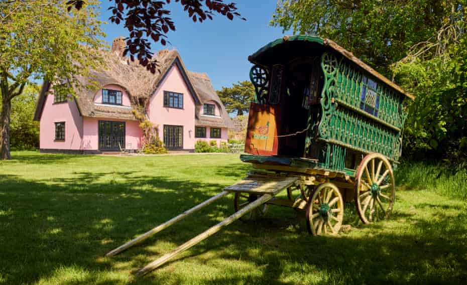 The pink exterior of the home of fashion designers Justin Thornton and Thea Bregazzi in Walberswick, Suffolk, with a green vintage caravan in front