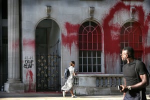 people walk past a building covered in red grafitti