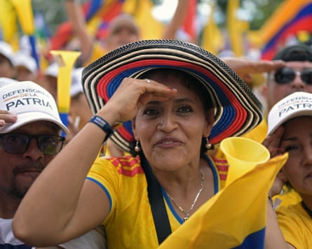 A woman wearing a shirt and wide-brimmed hat in the colours of the Colombian flag salutes at the camera