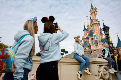 Visitors wearing Mickey and Minnie Mouse ears take selfies in front of castle