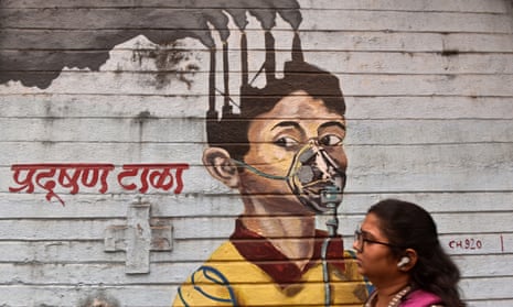 A woman walks past a mural painting of pollution on a wall in Mumbai, India