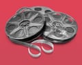Two metal film reels with unspooled film strips rest together against a red background