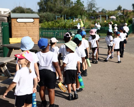 Pupils wearing hats and holding water bottles stand in a line outdoors