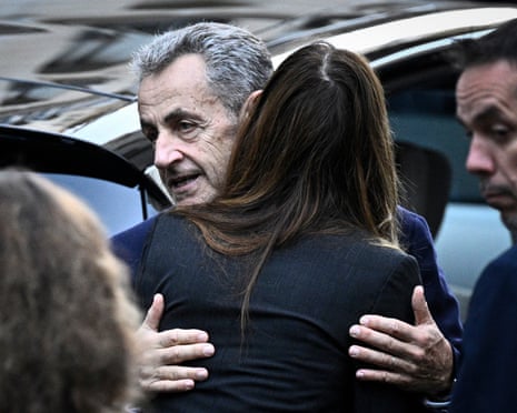 France’s former president Nicolas Sarkozy hugs his wife, Carla Bruni-Sarkozy, as he leaves his residence to present himself to La Sante prison for incarceration on a five-year prison sentence after being convicted of criminal conspiracy over a plan for late Libyan dictator Moamer Kadhafi to fund his 2007 electoral campaign, in Paris, on 21 October 2025.