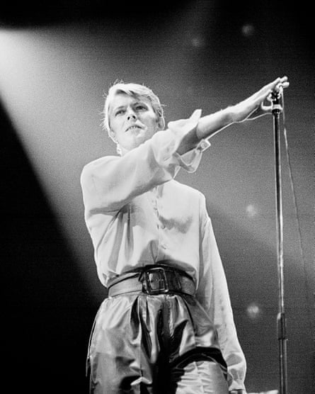A black and white image of Bowie holding the mic away from his face and staring into the crowd