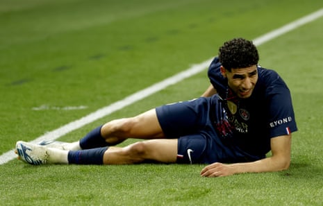 Achraf Hakimi of PSG lies on the pitch holding the back of his leg.