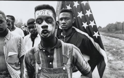 A young civil rights marcher with "VOTE" written on his forehead, an American flag behind him