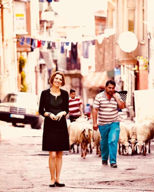 Elif Shafak in a street in Istanbul with a flock of sheep behind her and washing hung over the street