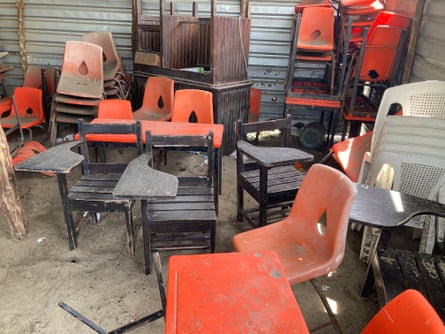School desks and chairs haphazardly piled up and covered in sand 