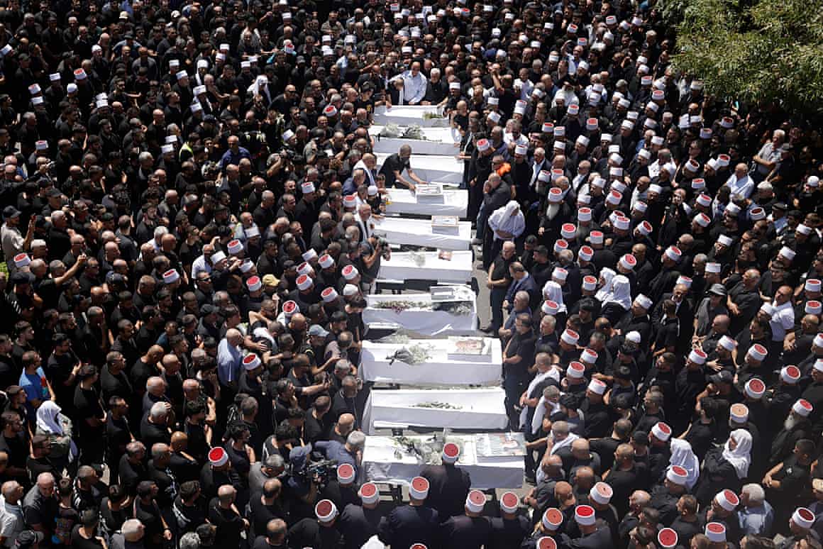 Mourners at a funeral with 10 coffins in the crowd