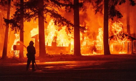 A firefighter sprays water as a house burns in the Dixie fire in the Indian Falls area of Plumas County, California.