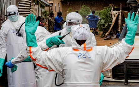 A health worker wearing full protective gear raises their hands in the air as another sprays them with disinfectant