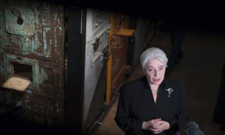 Natalia Solzhenitsyn stands in darkness in front of replica cells and cell doors; she wears black and is addressing media