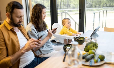 Parents and a baby using smartphones and tablets at the kitchen table
