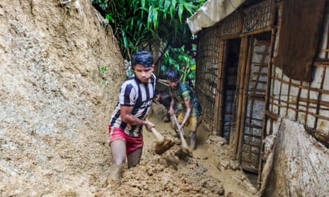 Rohingya refugees shovel mud from outside a bamboo and tarpaulin shelter after the floods