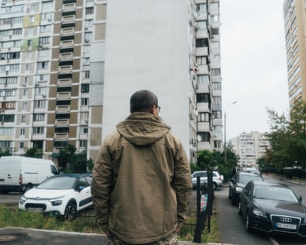 A man stands with his back to the camera in a residential neighbourhood of high-rise blocks