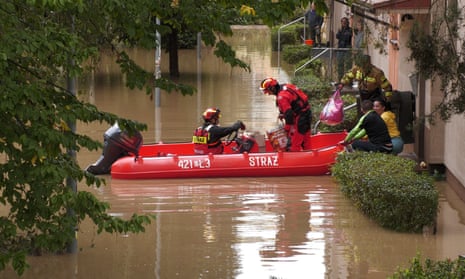 People stand on their doorsteps as a rescue boat moves along a flooded street