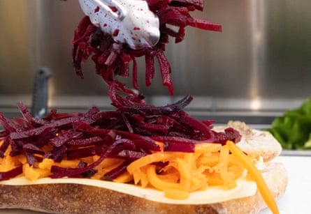 A pair of tongs arranging julienned beetroot on a salad sandwich