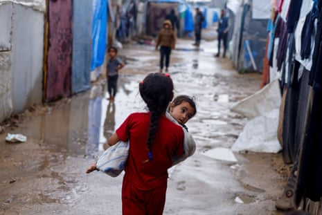 A displaced Palestinian girl holds a child as she walks in a tent camp on a rainy day in Rafah, 6 May.
