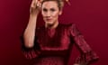 Grace Dent wearing a shiny, dark red version of the Falconetti dress: it has pointed shoulders, a high neckline and ruffles at the elbow. Grace is pictured from the waist up holding one hand high and is photographed on a dark red background, against which the dress glitters.