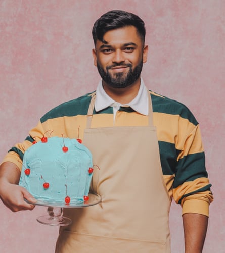 A dark-haired young man holds up a blue cake with red cherries on it.