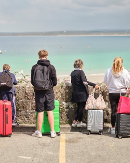 People standing with cases, backs to the camera, on the seafront in St Ives, Cornwall, UK, July 2024