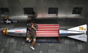 A man lights a cigarette on a bench in a shape of a mock aerial bomb outside a fashion boutique selling U.S. brand clothing at a mall in Beijing.