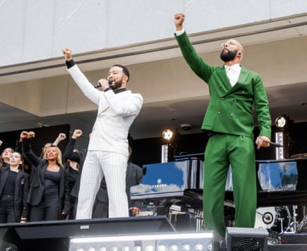 Two men in suits singing and raising their right fists to the sky.