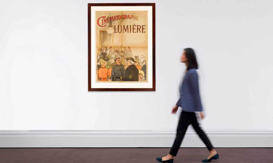 Woman walks past poster for Lumière brothers short film in gallery