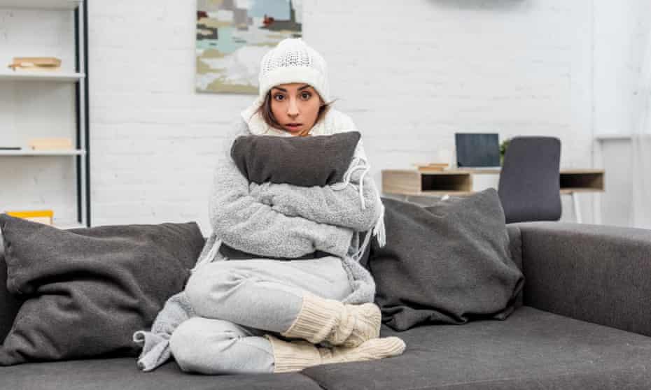 Freezing young woman in warm clothes sitting on couch and hugging cushion