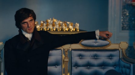 Jacob Elordi sitting on a blue chair in a scene from Wuthering Heights.