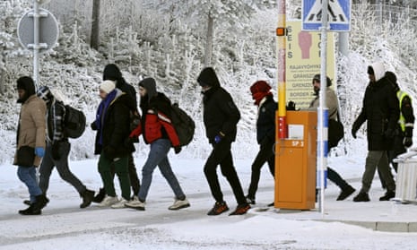 People walk through a raised barrier gate amid a snowy landscape