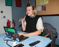 A young blond woman sits at a blue desk at a laptop.