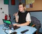 A young blond woman sits at a blue desk at a laptop.