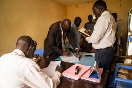 A group of men in suits pore over documents in a small room.
