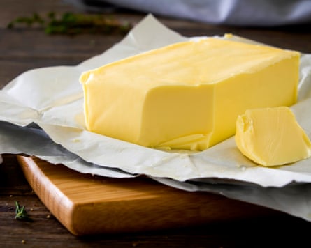 Close up shot of a block of butter on a chopping board, cut with a knife on a rustic wooden kitchen table