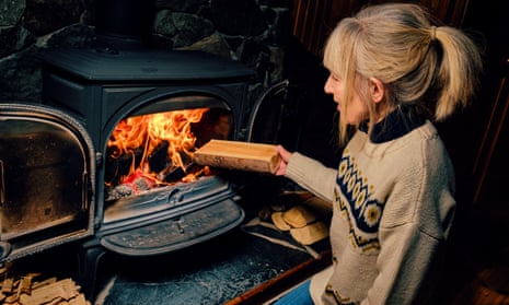 Woman putting a log on a wood-burning stove.