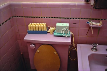 A pink bathroom showing a sink with silver taps, and a toilet console with yellow heated rollers and a small light green sewing machine on top