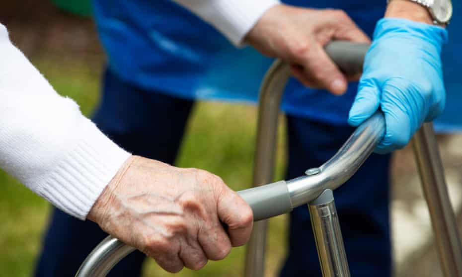 A carer helps a care home resident using a walking frame