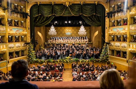 People watch a performance in the opera house. Much of the interior is decorated in gold leaf, while paintings on exteriors of audience boxes include flowers, and cherubs with musical instruments or in playful mood