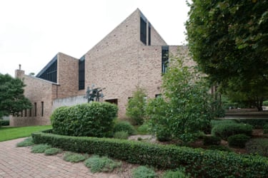 Clubbe Hall’s brick exterior with angular rooflines stands behind landscaped hedges and trees