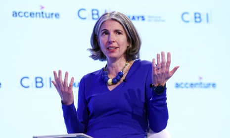 Rain Newton-Smith onstage at an event in a blue outfit, seated and gesturing with both hands, in front of a backdrop decorated with corporate logos