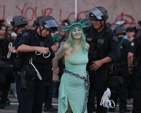 Two police officers use tape to handcuff a defiantly smiling woman dressed as Liberty in Chains